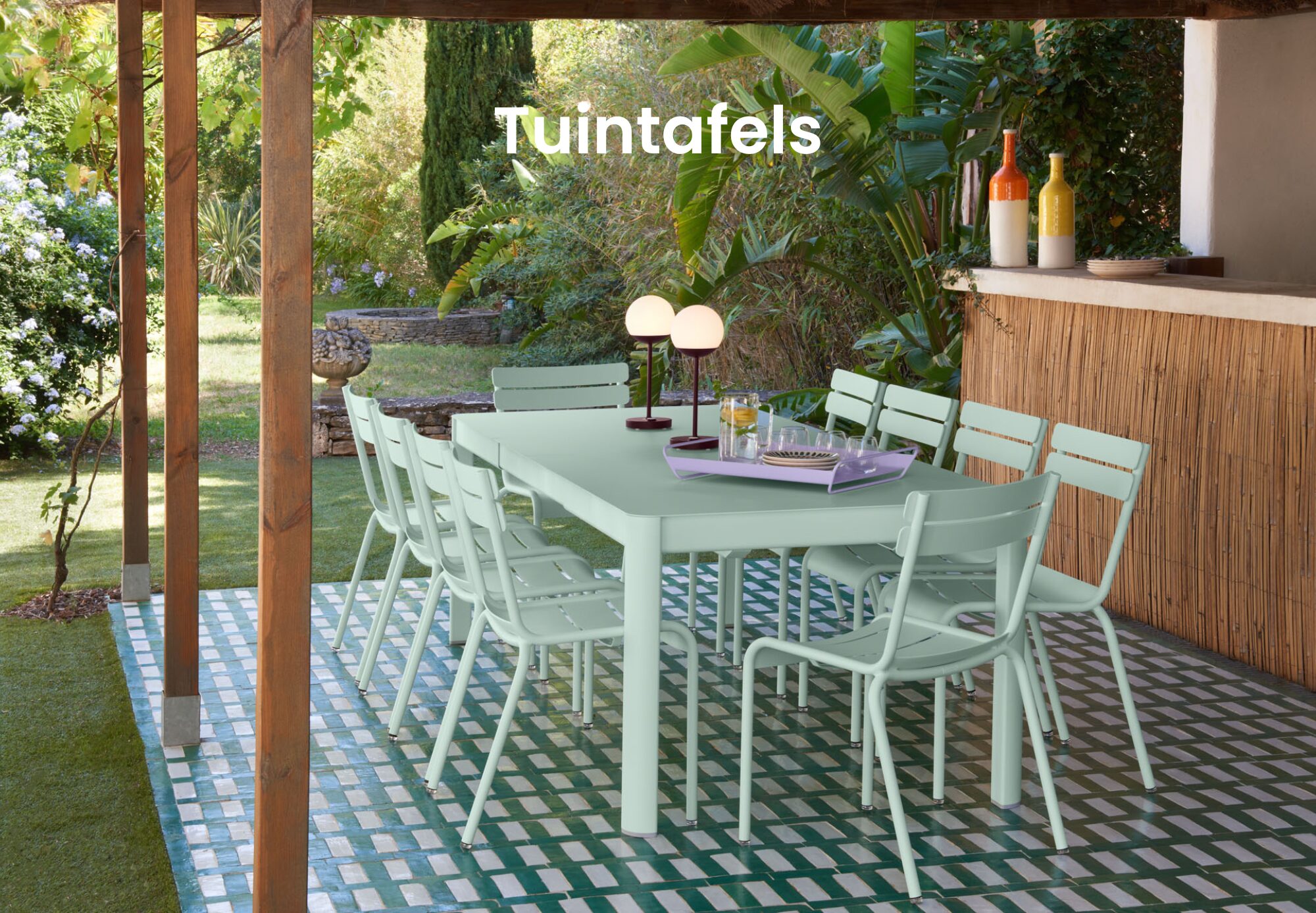 Une grande table à manger d'extérieur vert menthe avec des chaises assorties de Quatuor Design se trouve sur un patio carrelé sous une pergola, entourée de plantes et de verdure de jardin - parfaite pour ceux qui recherchent l'inspiration en matière de design de magasin de meubles.