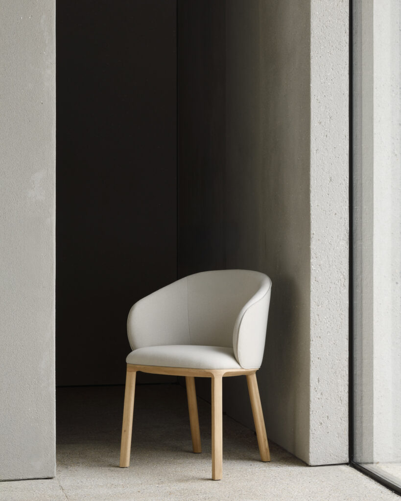 Une chaise de salle à manger moderne en chêne beige rembourrée avec des pieds en bois est placée dans le coin d'une pièce minimaliste près d'une grande fenêtre.