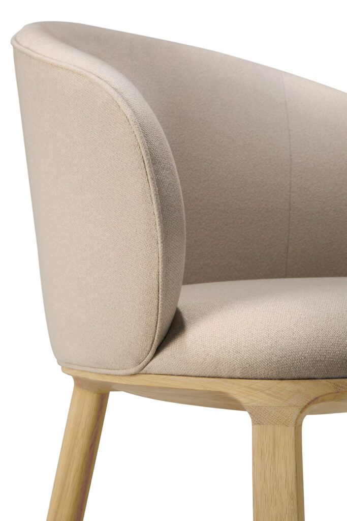 Une chaise de salle à manger Unda rembourrée beige avec des pieds en bois, présentée sous un angle latéral sur un fond blanc.