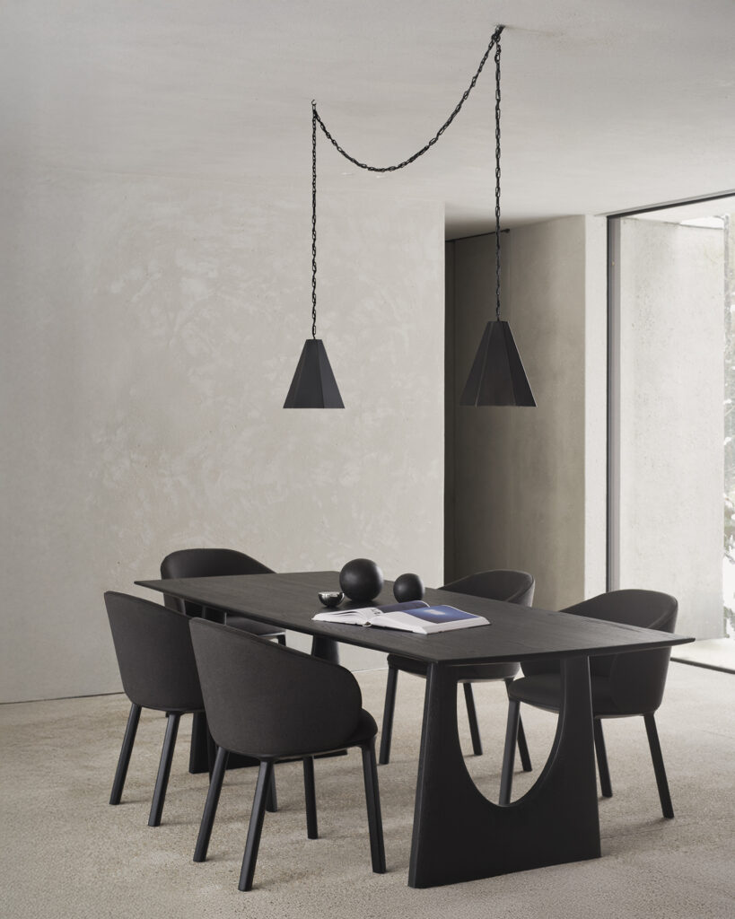 Salle à manger minimaliste avec une table noire, six chaises de salle à manger Unda, deux suspensions géométriques noires et des accents de décoration, sur fond de murs à texture claire et de moquette.