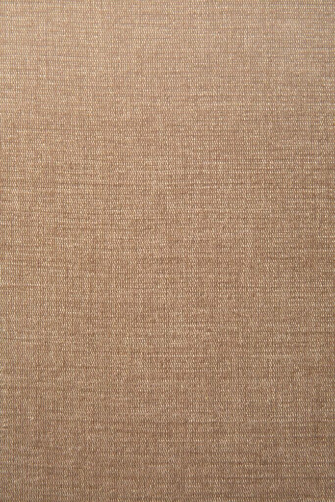 Gros plan d'une surface de tissu beige avec une texture tissée fine et visible et une couleur uniforme, parfaite pour tapisser un canapé volumineux.