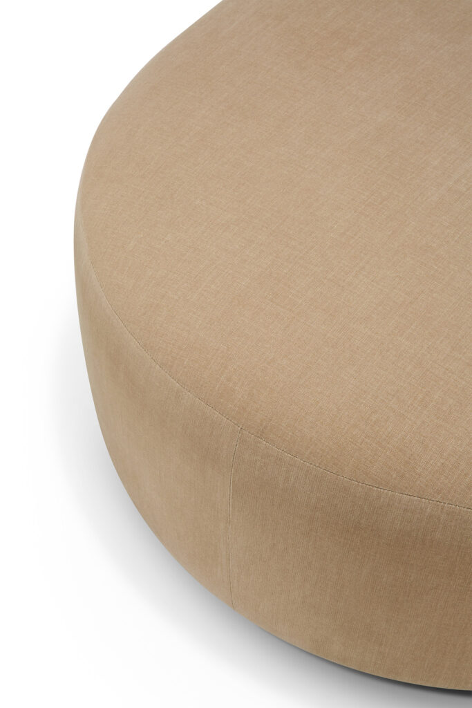 Vue rapprochée d'un pouf rond, volumineux et rembourré de couleur beige, posé sur un fond blanc.