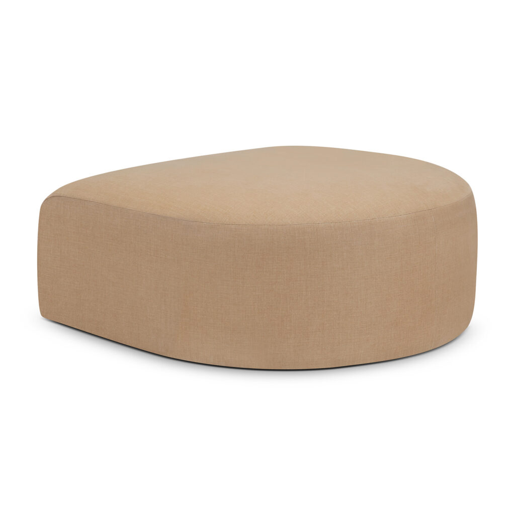 Un pouf recouvert de tissu marron clair, de forme légèrement volumineuse, arrondie et asymétrique, repose sur un fond blanc.