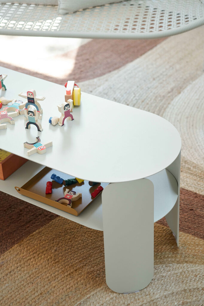 La Console basse Bebop, une table basse blanche moderne, présente des jouets en bois à empiler et un plateau de petites figurines d'animaux sur un tapis à motifs beige et marron, apportant le charme Bebop à la pièce.