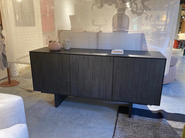 L'Expo - Buffet Mosaic se compose de bois foncé et de portes texturées, posées sur un sol en béton au milieu d'un mobilier neutre et d'un éclairage doux, pour un look moderne et saisissant.