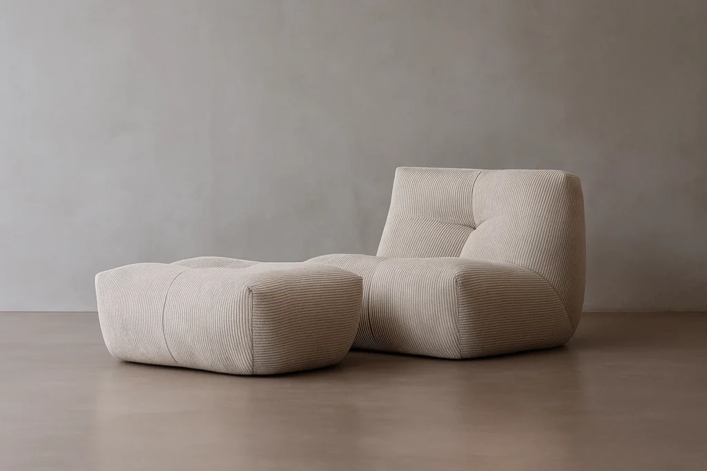 Un fauteuil moderne beige Cozy S - 1 place avec ottoman est posé sur un sol marron lisse contre un mur gris uni.