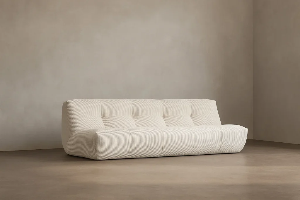 Le Cozy S - 3 places, un canapé touffeté moderne de couleur crème aux courbes douces, est adossé à un mur beige dans une pièce minimaliste au sol lisse.