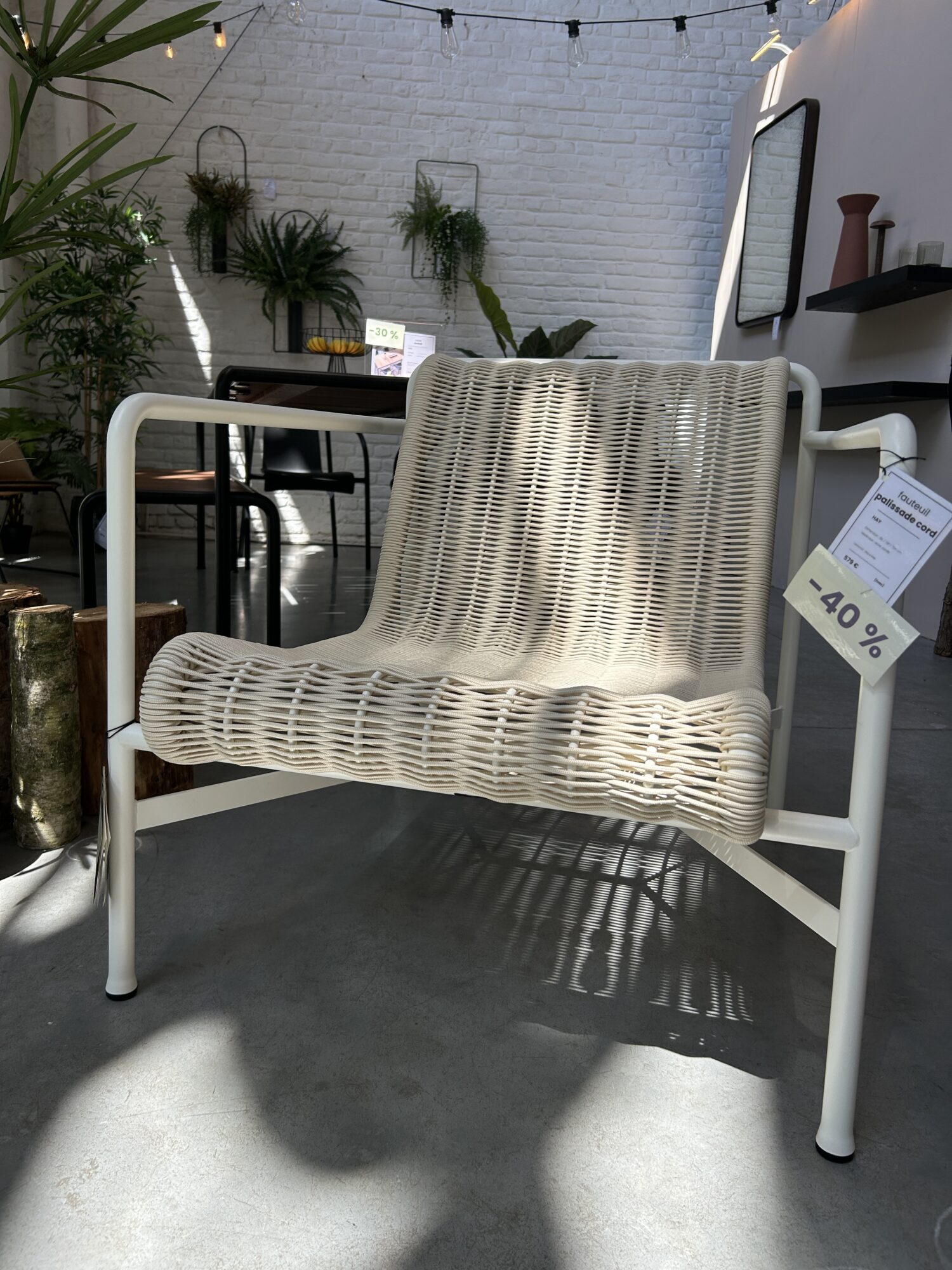 L'Expo - Fauteuil bas Palissade Cord, un fauteuil de salon tissé blanc avec un cadre en métal, est présenté à l'intérieur avec un décor moderne et des plantes en arrière-plan. Une étiquette de vente indique une réduction de 40 %.