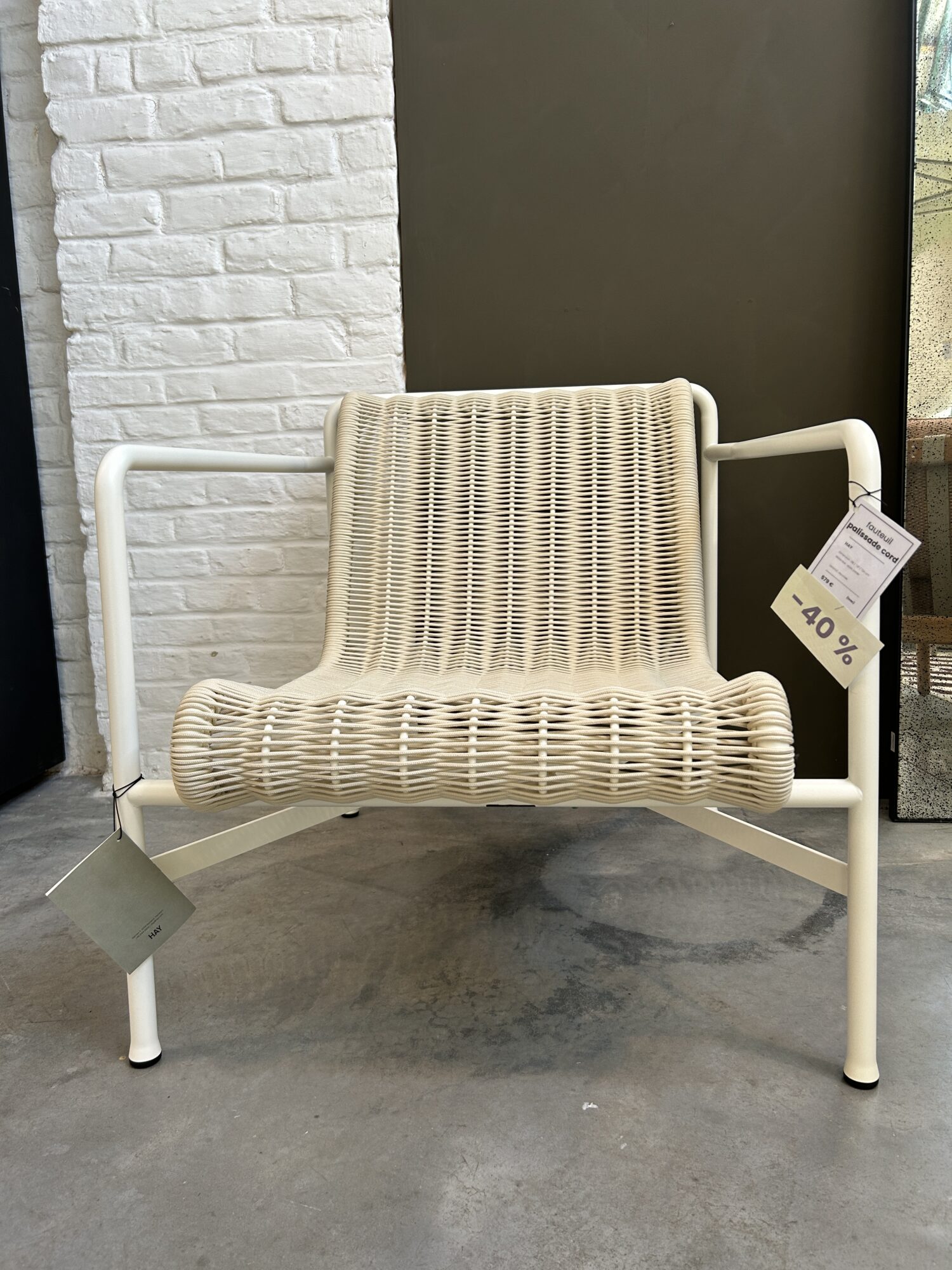 L'Expo - Fauteuil bas Palissade Cord, une chaise moderne en métal blanc avec une assise et un dossier en corde tressée, est exposée à l'intérieur sur un sol en béton avec une étiquette de réduction de 40 %.
