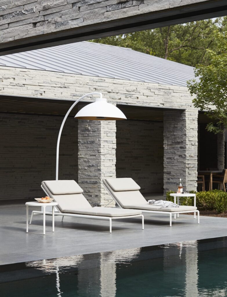 Deux chaises longues beiges sont installées au bord d'une piscine sous une grande lampe dôme blanche, avec une petite table d'appoint contenant des boissons et des snacks, le tout contre la façade moderne en pierre du DOME FS, créant ainsi une retraite de minuit invitante.