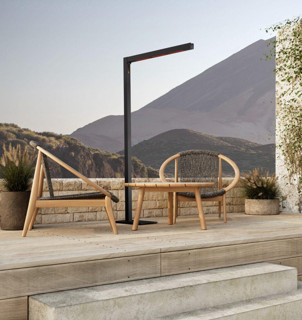 Deux chaises d'extérieur en bois et un lampadaire moderne TWIG FS - Midnight (230V, EU) sont disposés sur un patio avec des marches en pierre, des plantes en pot et des montagnes lointaines sous le ciel de minuit.