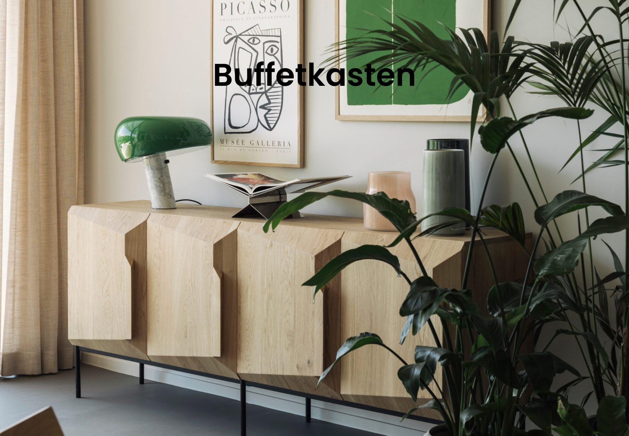 Un buffet en bois clair de Quatuor Design avec des portes géométriques, des objets de décoration verts et beiges, des plantes d'intérieur et des œuvres d'art encadrées crée un look moderne, avec le mot "Buffetkasten" au-dessus - parfait pour les amateurs de meubles design.