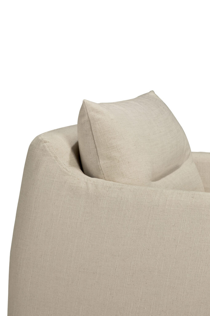 Gros plan sur l'angle d'un canapé rembourré de couleur os avec un coussin assorti, placé à côté d'une chaise longue confortable, sur un fond blanc.