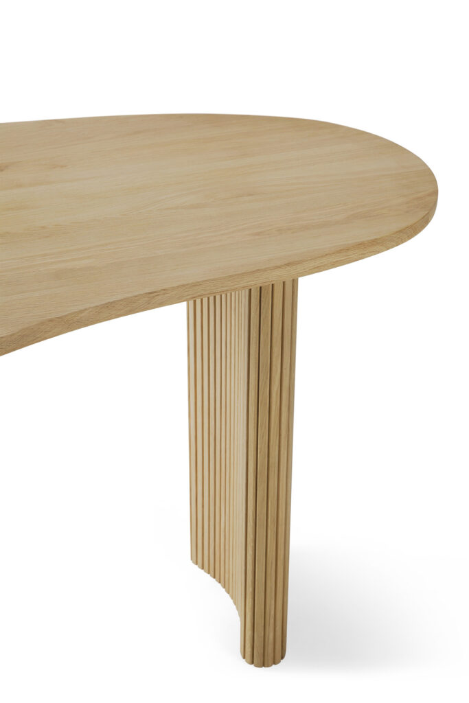 Gros plan sur une table en bois clair, en chêne naturel, avec un bord arrondi et un pied incurvé et rainuré verticalement, un détail élégant de la collection Bureau Boomerang.