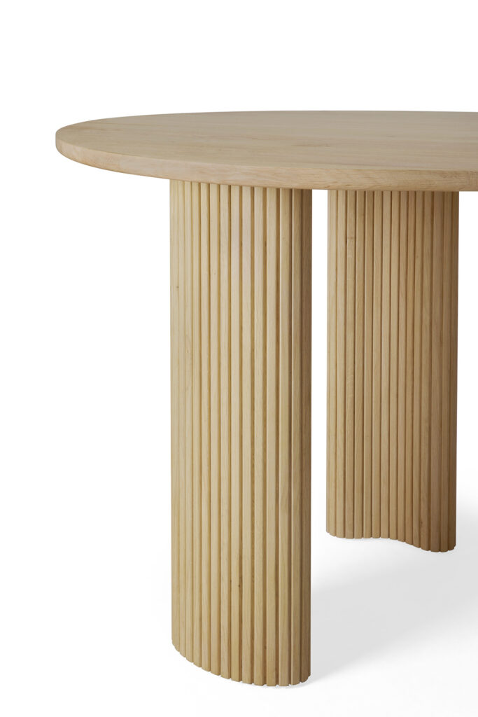 Table ronde en bois chêne naturel avec pieds cylindriques cannelés et finition vernis lisse, présentée sur fond blanc.