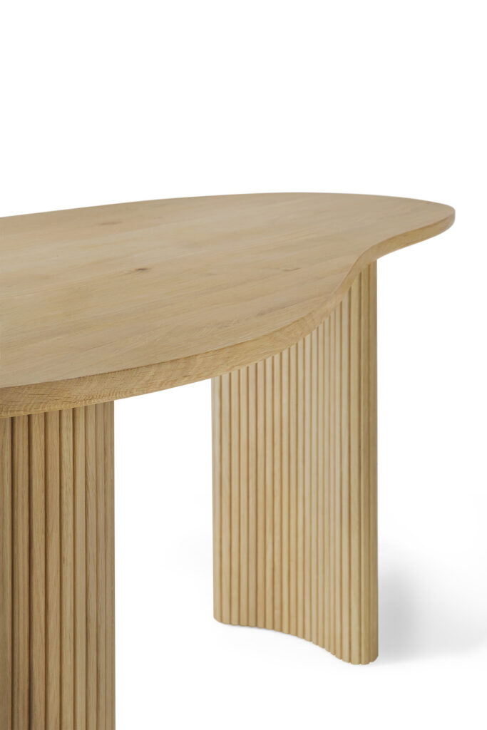 Table Bureau Boomerang en bois chêne naturel à bord arrondi et pieds verticaux cannelés, vue de côté en biais sur fond blanc.