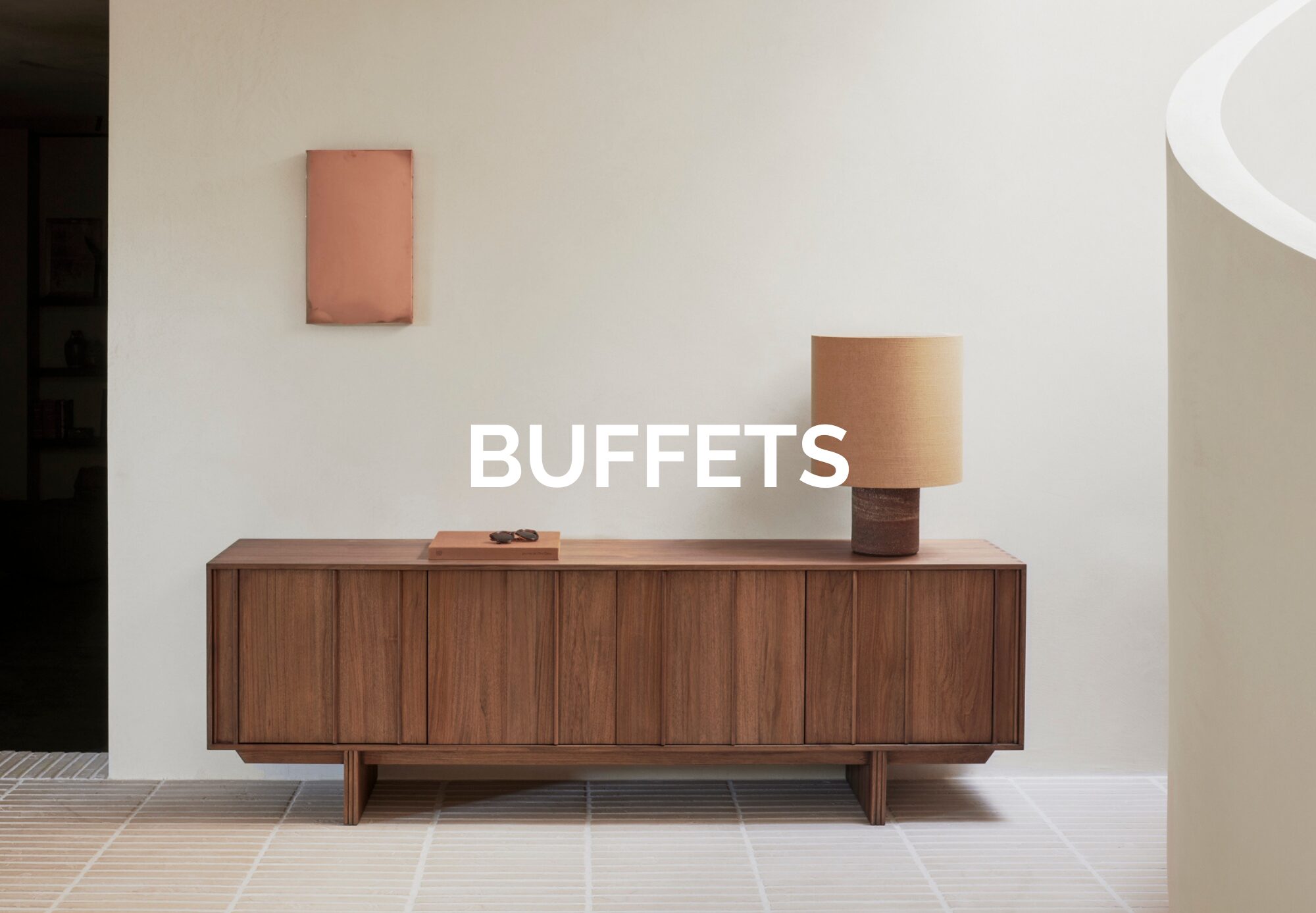Table de buffet en bois de Quatuor Design, surmontée d'une lampe et d'un objet décoratif, placée contre un mur de couleur claire. Le mot "BUFFETS" est superposé en texte blanc, dans le style d'un magasin de meubles.