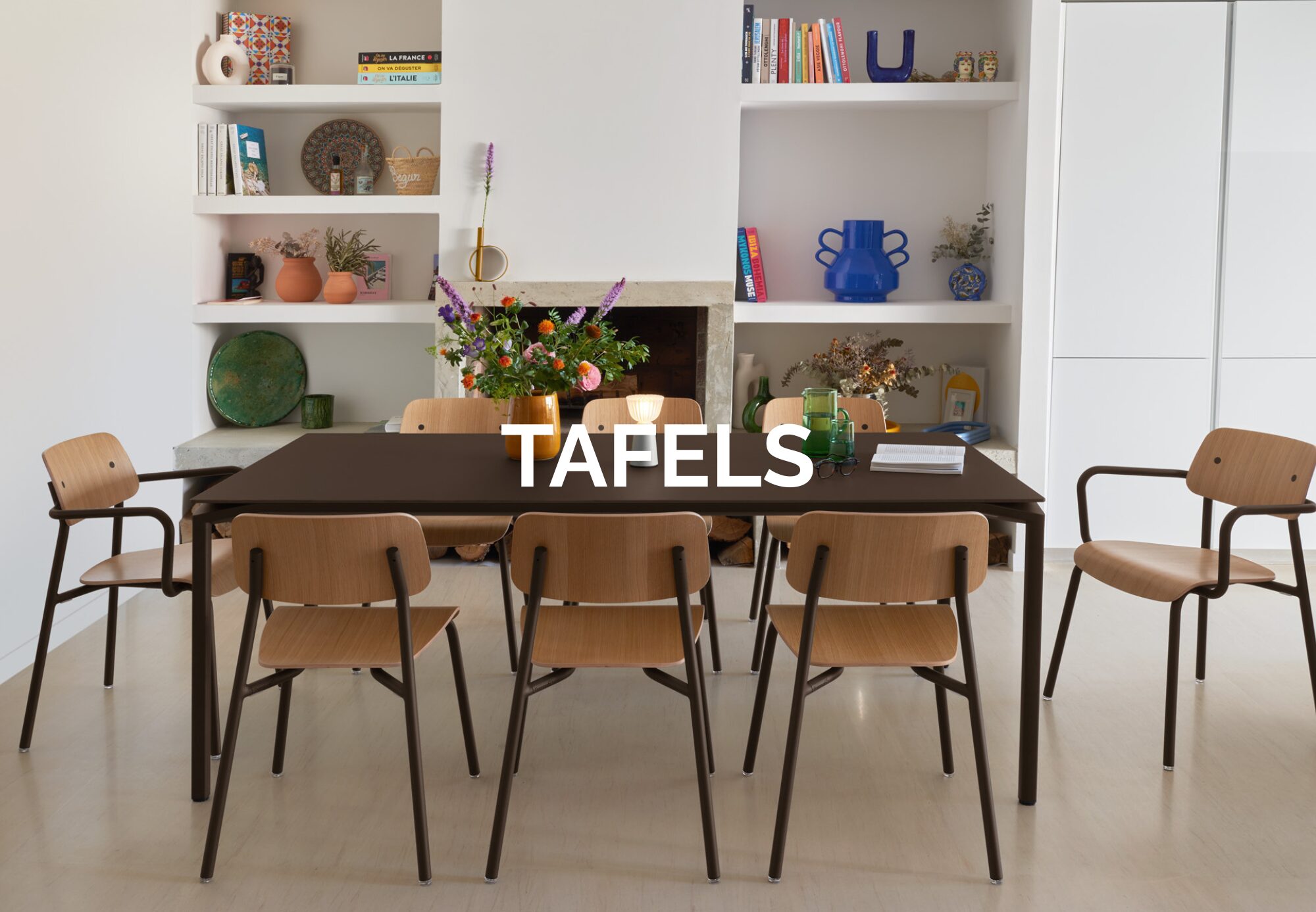 Une salle à manger moderne avec une table sombre, six chaises en bois de Quatuor Design, des fleurs et des étagères en arrière-plan. Le mot "TAFELS" est centré sur l'image, mettant en évidence les meubles de style.