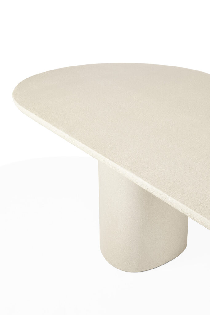 Une table beige, asymétrique et oblongue, avec une surface lisse et un socle arrondi unique - mettant en valeur des éléments de table uniques - se détache sur un fond blanc.