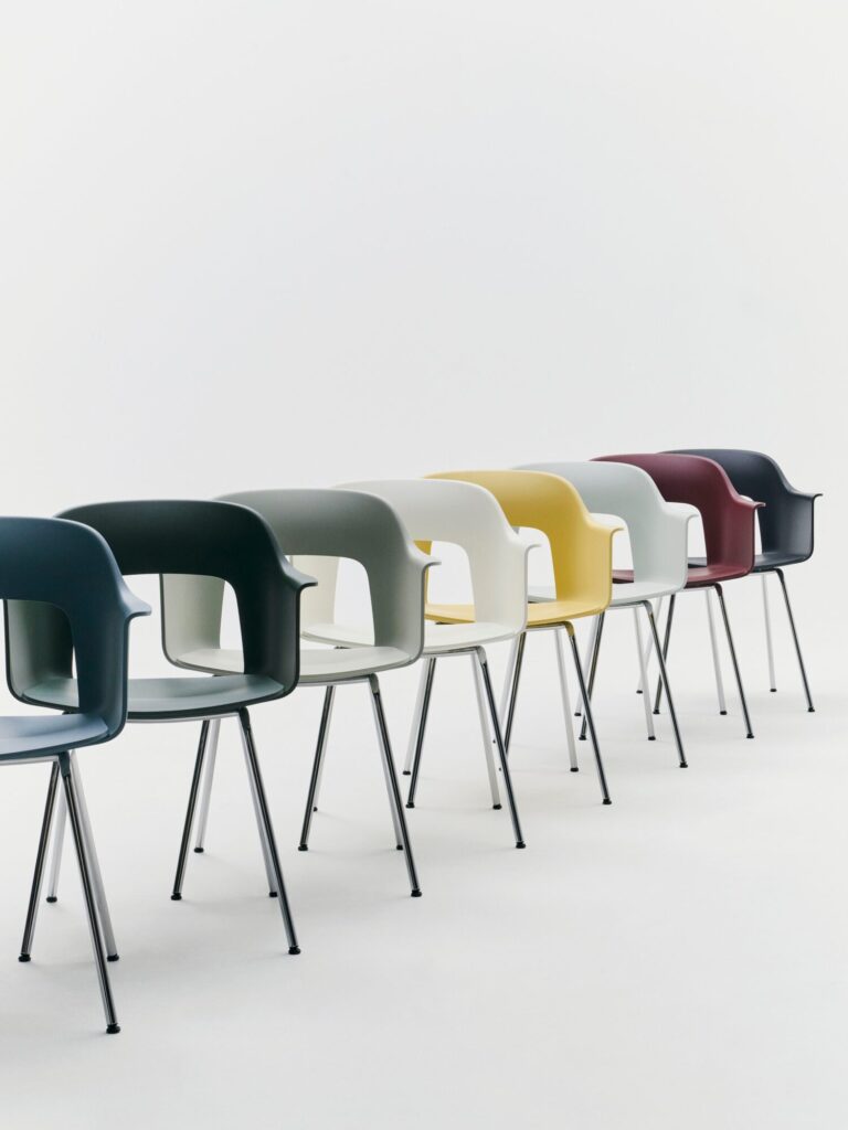 Six chaises modernes en plastique Layout avec des pieds en métal sont disposées en rangée, chacune dans une couleur différente : bleu foncé, vert, gris, blanc, jaune et rouge, sur un fond blanc uni.