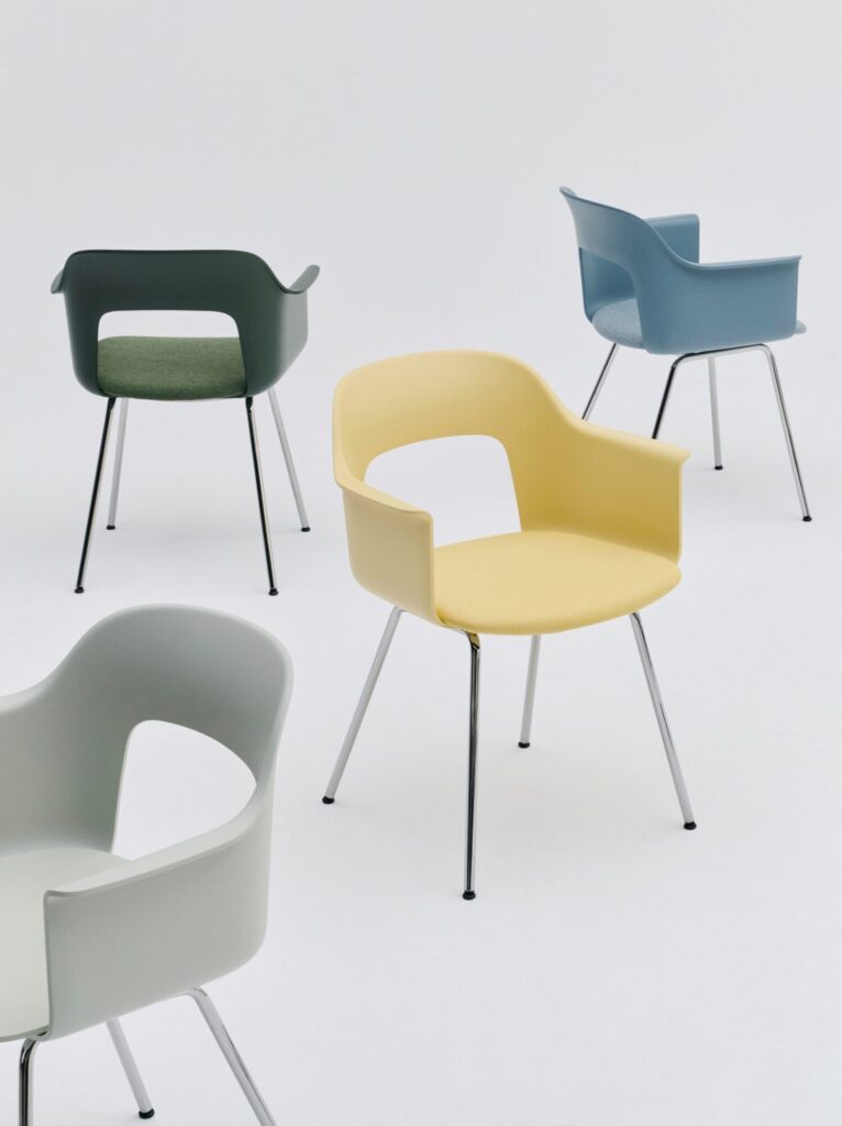 Quatre fauteuils "Layout" en vert pâle, jaune, bleu et vert foncé avec des pieds en métal et un design minimaliste sont disposés sur un fond blanc.