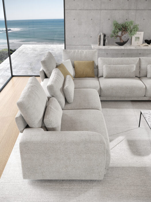 Salon moderne composé d'un Canapé Willow [4z-Nzz-4z] - C25 Perfect Harmony gris clair, de coussins beige et or, d'une table basse en marbre et de grandes fenêtres avec vue sur l'océan.