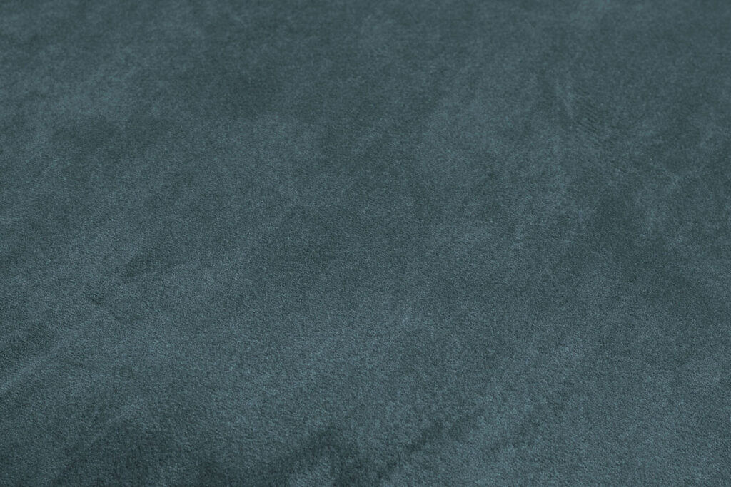 Gros plan sur la surface texturée d'un tissu vert foncé à l'aspect doux et velouté, rappelant les matériaux recyclés en velours.