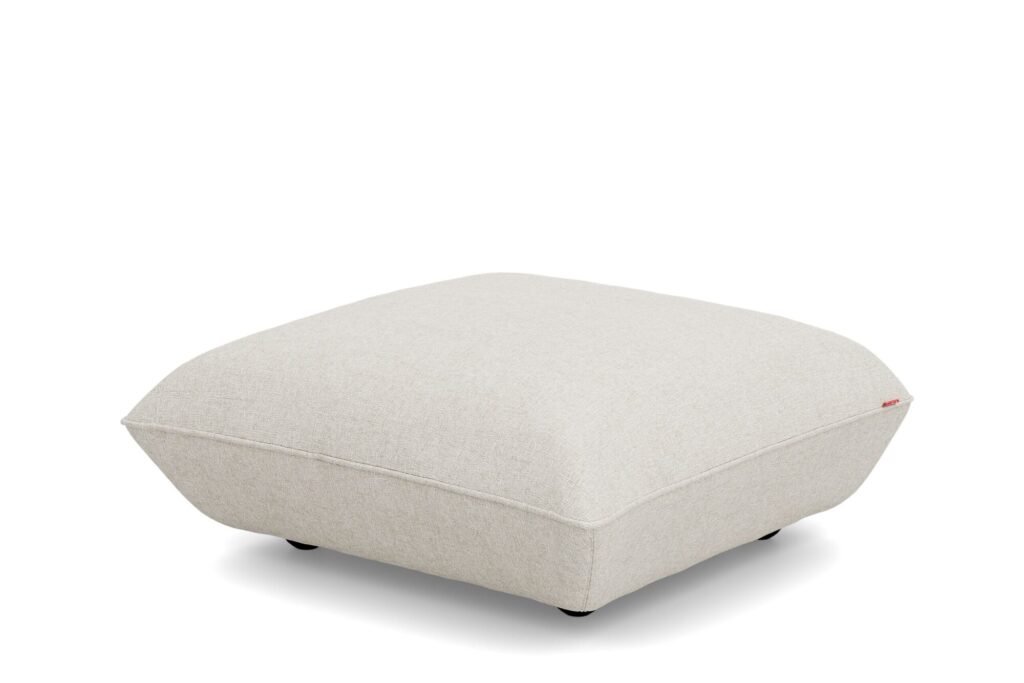Ce pouf carré beige clair, recouvert d'un tissu bouclé doux et aux bords arrondis, repose sur de petits pieds noirs sur un fond blanc uni. Inspiré du design Sumo Hocker, il est à la fois élégant et confortable.