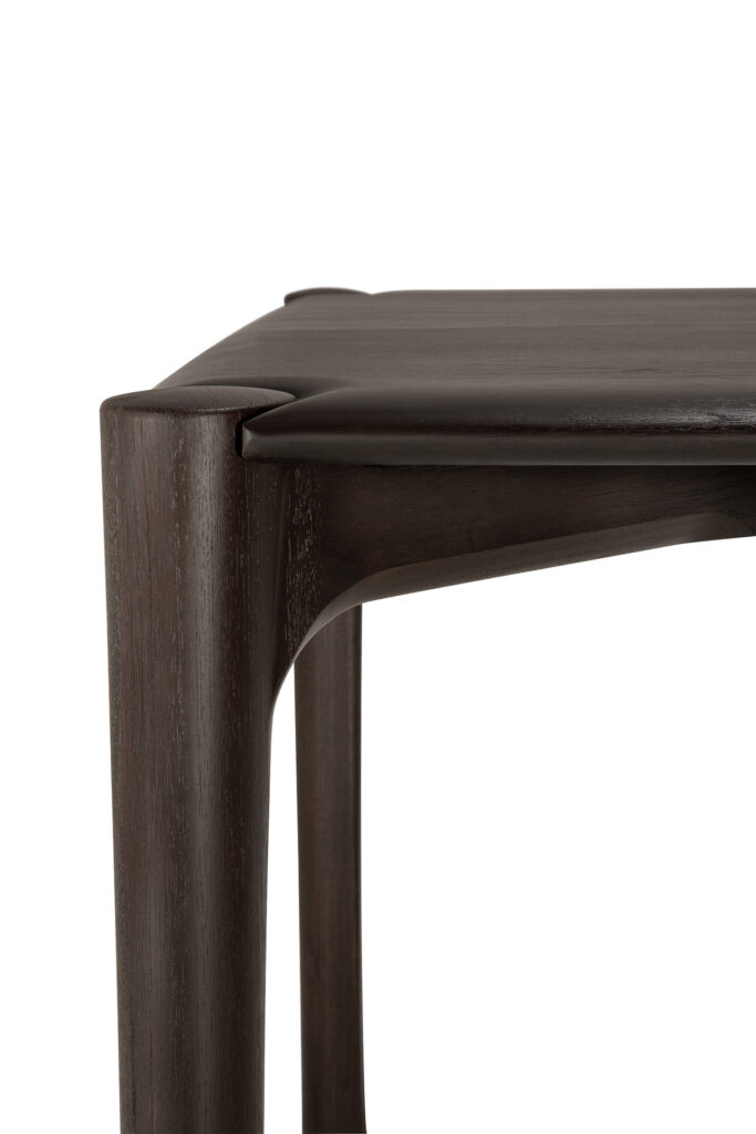 Gros plan sur le coin d'une table de salle à manger PI en bois foncé, aux bords arrondis et lisses, et dont les joints sont sans soudure.