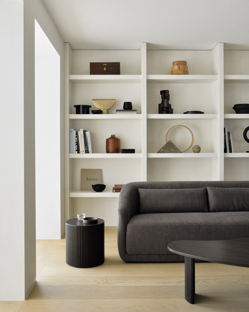 Un salon moderne composé d'un canapé gris foncé, d'une table d'appoint ronde Roller Max et d'étagères encastrées blanches présentant des livres, des céramiques et des objets décoratifs.