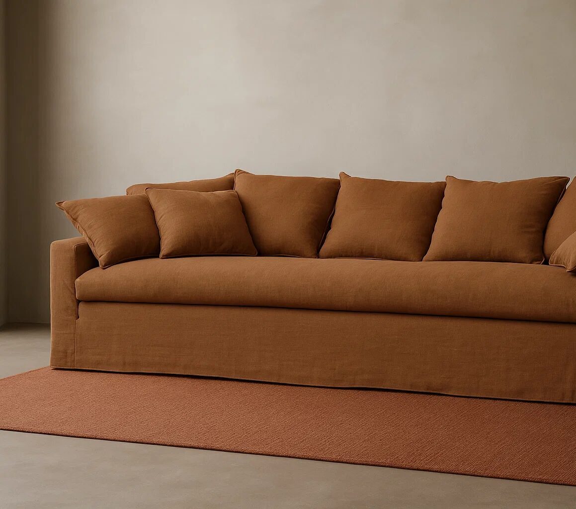 Un canapé capitonné marron avec cinq coussins assortis est posé sur un tapis marron contre un mur beige uni.