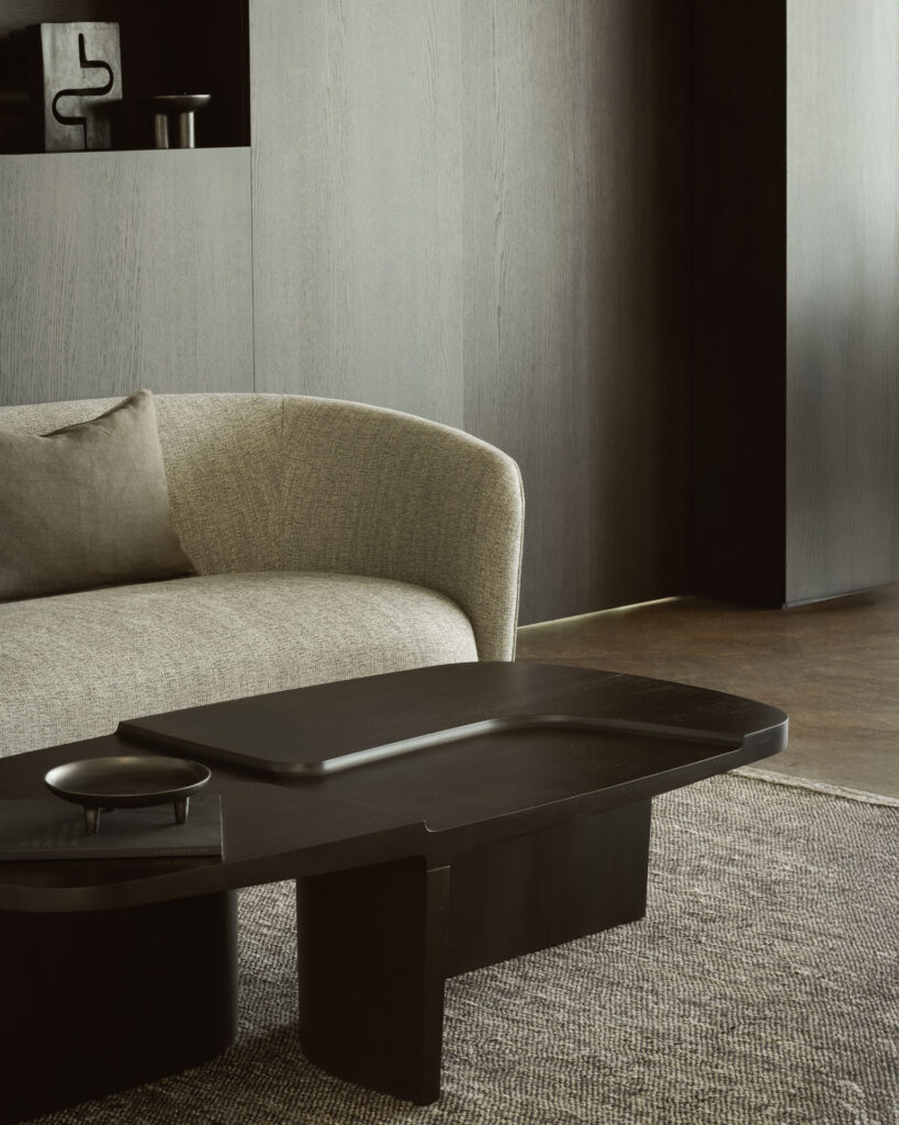 Un salon moderne avec la table basse Brutalist, un canapé beige incurvé et un tapis texturé sur un sol en bois.