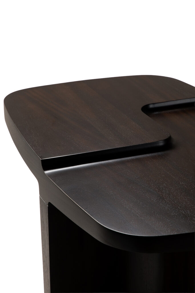 Un gros plan de la table d'appoint Brutalist montre son bois sombre, ses bords arrondis et lisses, ainsi qu'une rainure caractéristique creusée dans la surface.