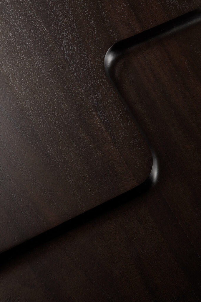 Gros plan de deux tables d'appoint d'inspiration brutaliste qui se chevauchent, en bois sombre aux bords arrondis, présentant un grain de bois subtil et un éclairage doux dans un design moderne d'inspiration brutaliste.