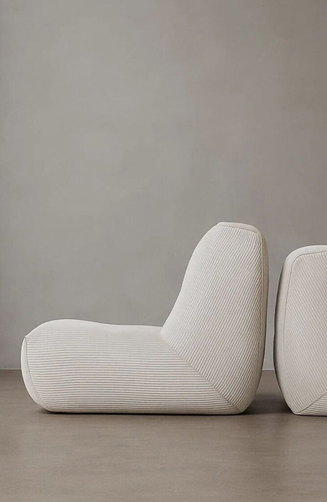 Une chaise longue moderne et discrète de couleur crème au design incurvé de Quatuor Design est posée sur un sol lisse contre un mur gris uni, ce qui est parfait pour tout magasin de meubles design.