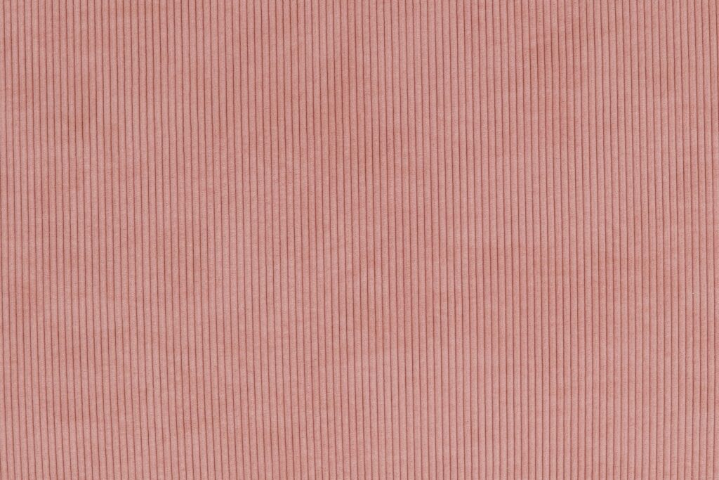Gros plan sur le tissu en velours côtelé rose du Sumo - Loveseat, mettant en valeur sa texture striée verticale et son aspect doux et confortable, idéal pour se détendre.