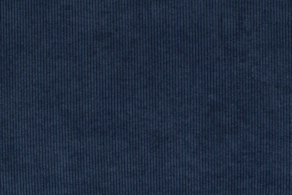 Gros plan sur un velours côtelé bleu foncé avec des stries verticales et une texture douce, parfait pour recouvrir le Sumo - Loveseat ou pour ajouter un confort moelleux à n'importe quel siège.