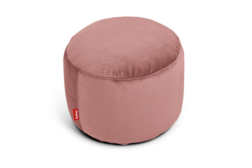 Un pouf rond en quartz rose fabriqué à partir de tissu recyclé en velours, avec une surface lisse et rose et une petite étiquette rouge sur le côté, sur fond blanc.