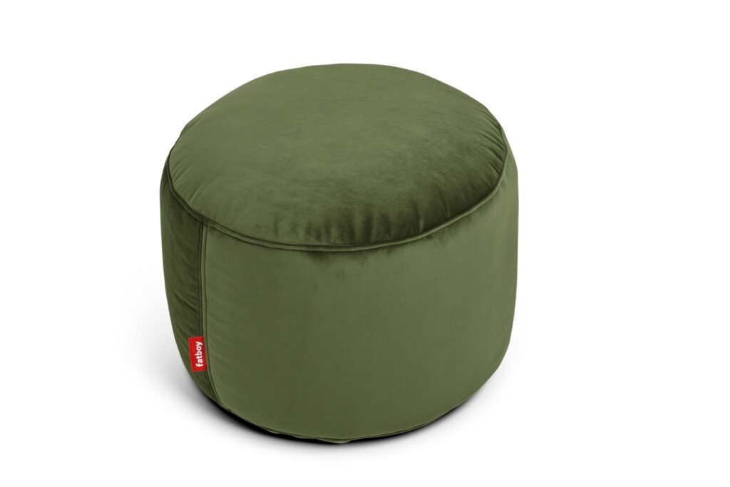 Un ottoman rond en velours vert foncé avec une finition douce et une petite étiquette rouge sur le côté, fabriqué à partir de tissu recyclé et présenté sur un fond blanc.
