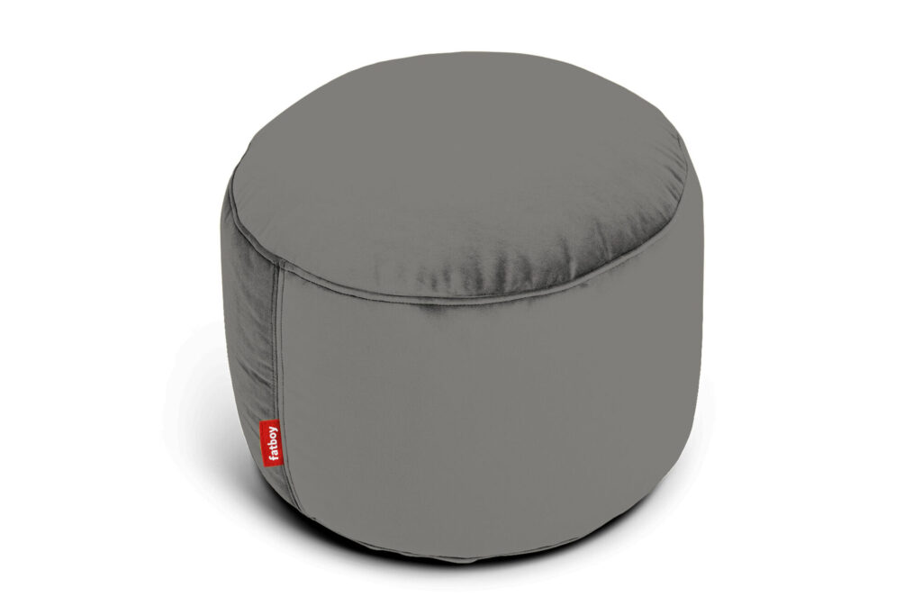 Un pouf rond en velours taupe recyclé avec une couture visible et une petite étiquette rouge attachée sur le côté, placé sur un fond blanc.