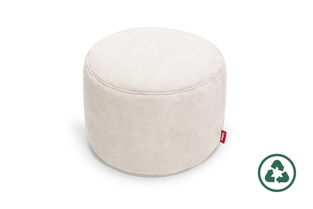 Un pouf Fatboy Point rond et crème avec une étiquette en tissu rouge est représenté à côté d'un symbole de recyclage vert sur fond blanc.