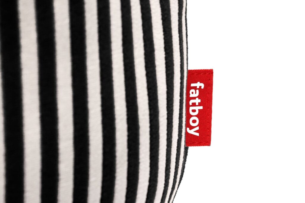 Gros plan sur un tissu rayé noir et blanc, semblable au style de Fatboy Point, avec une petite étiquette rouge portant la mention "fatboy" attachée sur le côté.