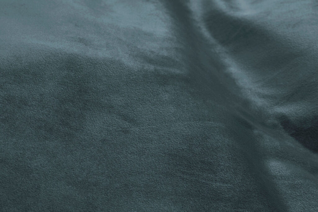 Gros plan sur la surface d'un tissu velouté recyclé sarcelle foncé, aux plis subtils et à la texture douce, parfait pour rehausser votre siège d'angle Sumo.
