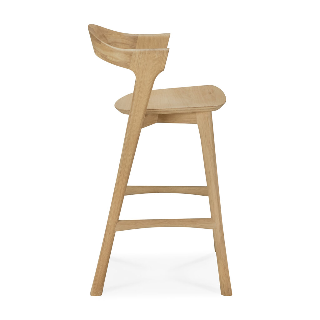 Vue latérale du Tabouret de bar Bok, un tabouret de bar moderne en bois avec un dossier incurvé, un repose-pieds et une finition naturelle claire, sur fond blanc.