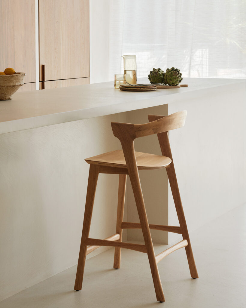 Un tabouret de bar Bok est placé sur un comptoir de cuisine minimaliste, accompagné d'un bol, d'un verre d'eau et de deux artichauts sur le comptoir épuré.