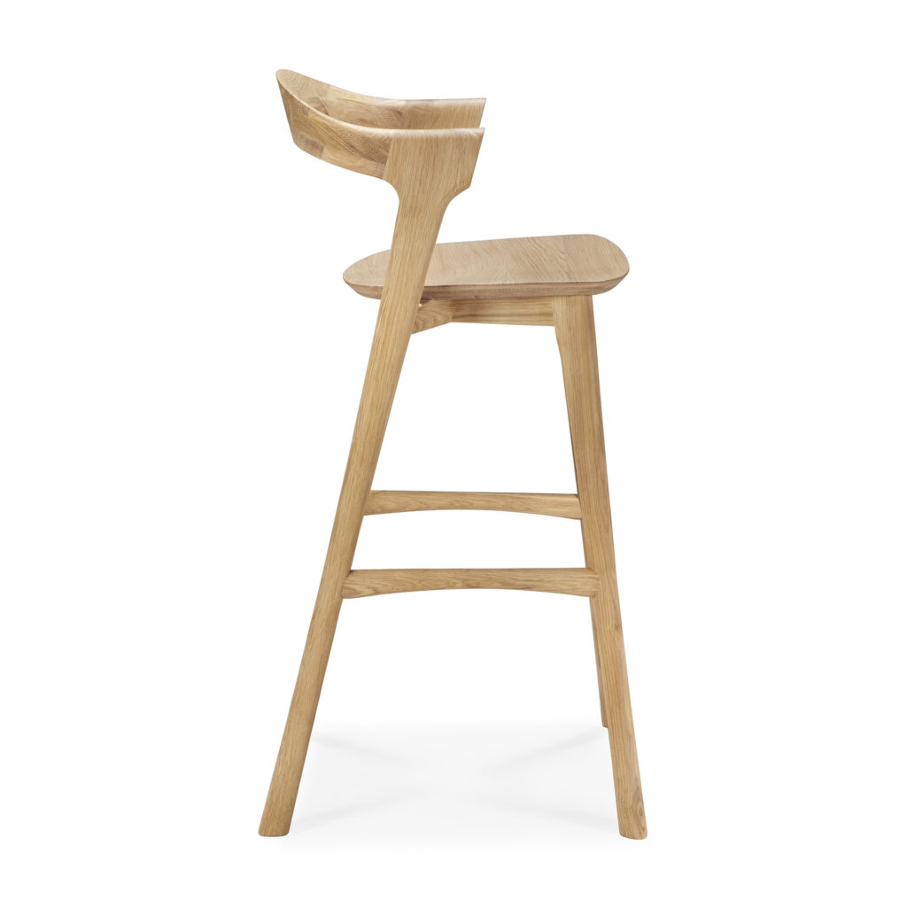Vue de côté du Tabouret de bar Bok, un tabouret de bar moderne en bois avec un dossier et un repose-pieds incurvés, avec une finition en bois clair naturel.