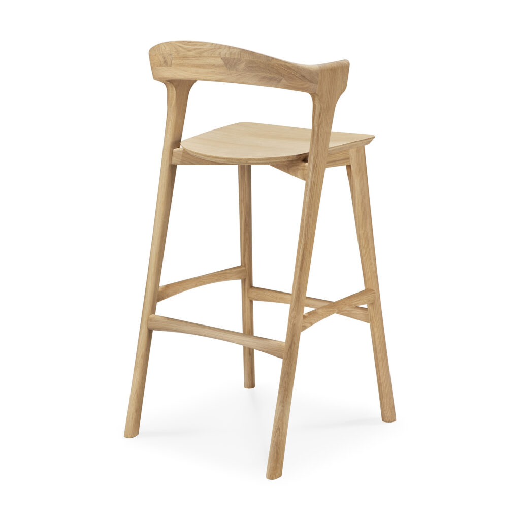 Le tabouret de bar Bok est un tabouret de bar en bois avec un dossier et un repose-pieds incurvés, au design minimaliste et à la finition en bois naturel.