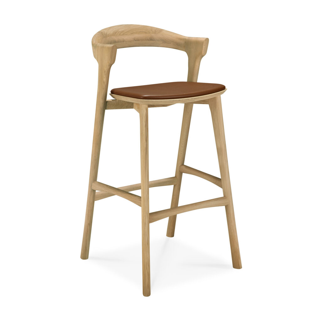 Le tabouret de bar Bok est doté d'une structure en bois, d'un dossier incurvé et d'une assise rembourrée de couleur marron. Ses pieds angulaires sont reliés par des supports horizontaux robustes, alliant confort et style pour tout type d'environnement.