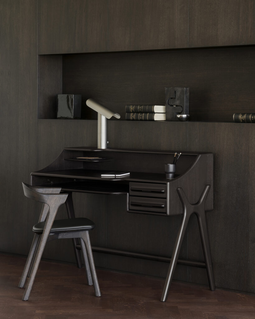 Bureau et chaise de style minimaliste en bois foncé, avec des étagères, des livres et une lampe de bureau blanche moderne, le tout placé contre un mur lambrissé assorti.