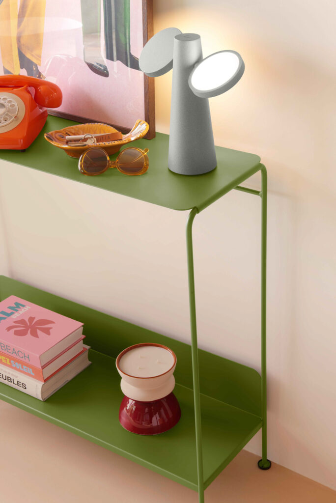 Une étagère verte Console Picolino présente une lampe grise, un téléphone orange, des lunettes de soleil, un cendrier, des livres et un égouttoir à café rouge et blanc - parfait pour un espace intérieur accueillant.